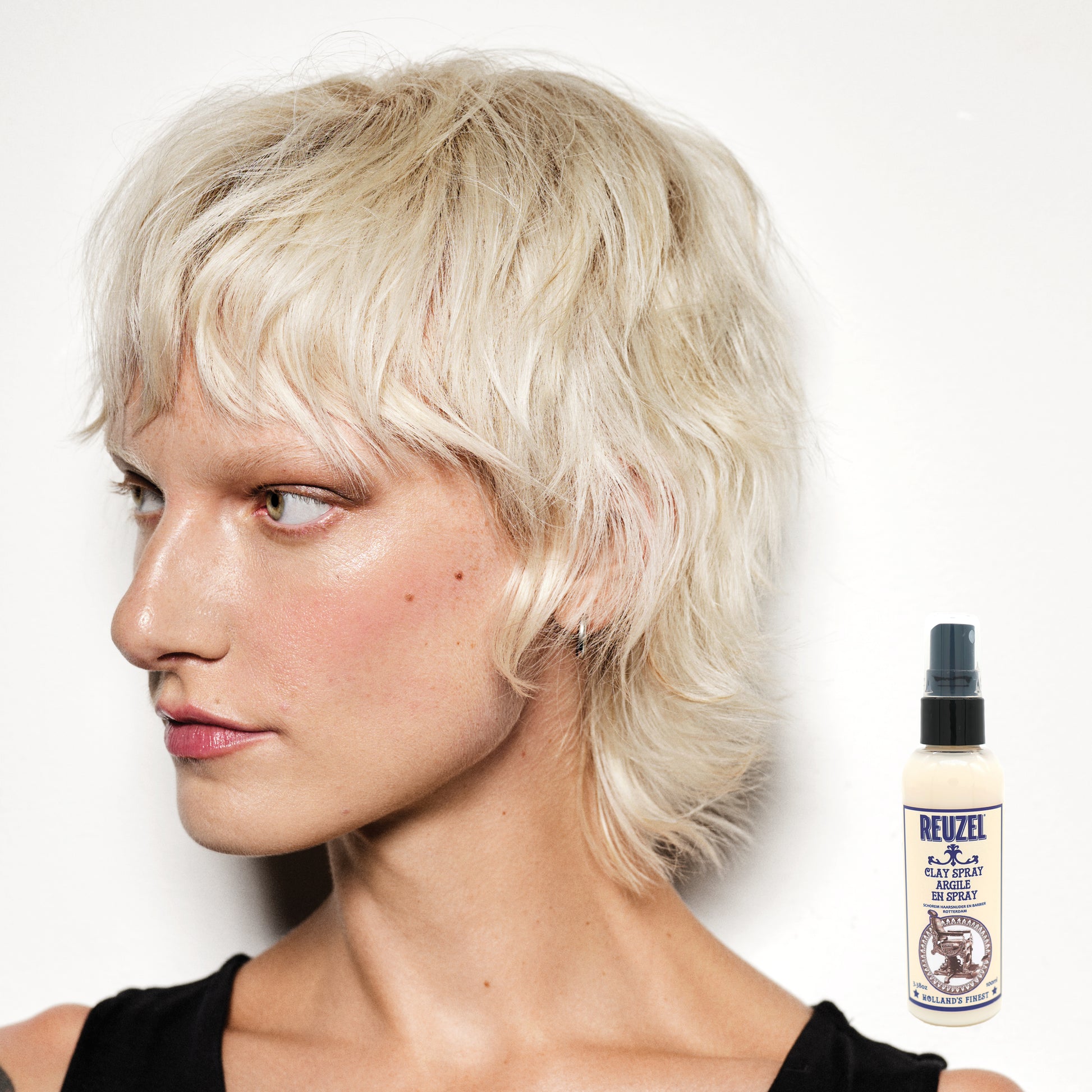 Reuzel Clay Spray hair styling product in a spray bottle, featuring a dark label with red and white accents.