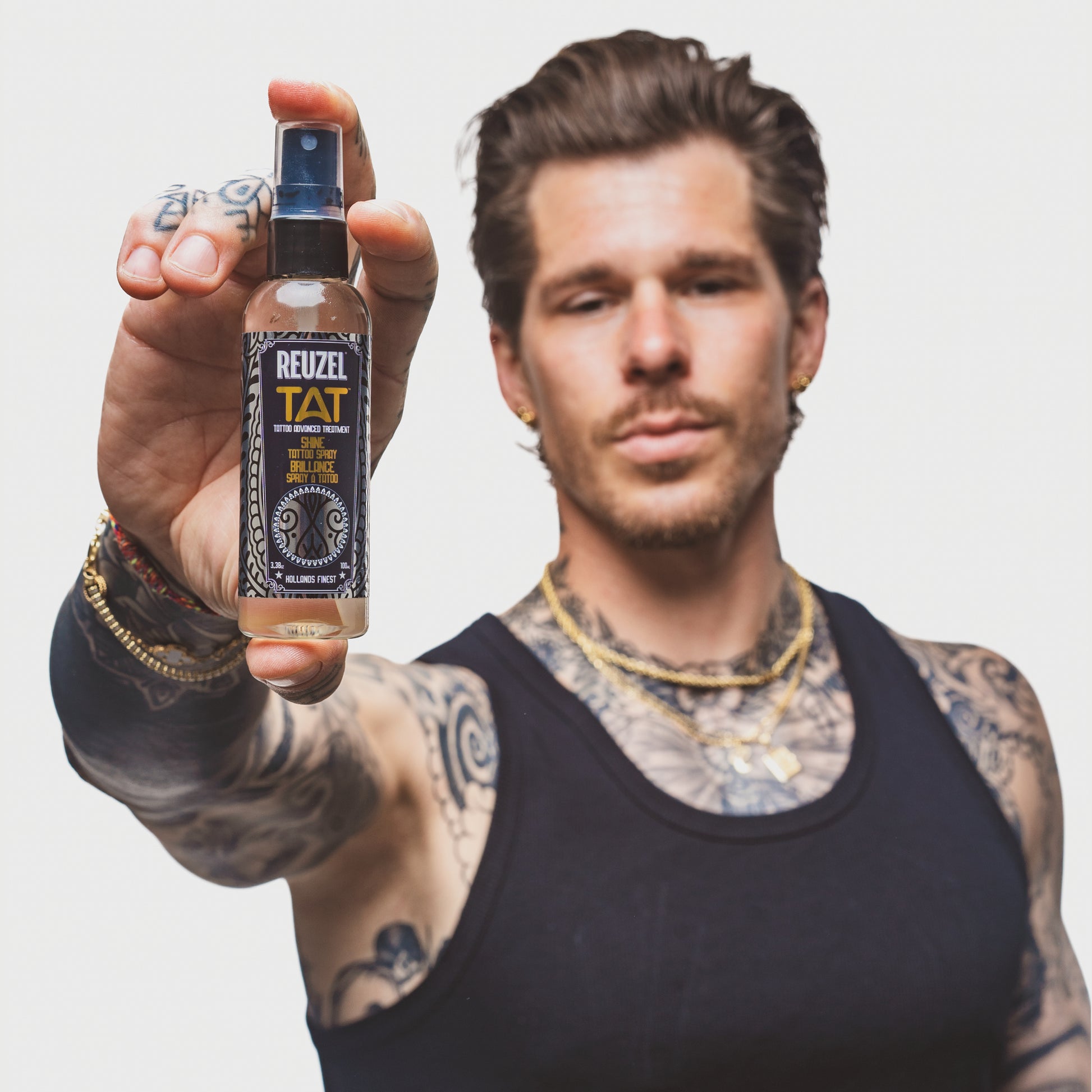 Person with tattoos holding a bottle of Reuzel TAT Shine Tattoo Spray